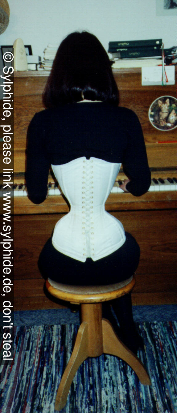 Satin corset 17 inch tightlaced to wasp waist at piano (back) Sylphide figure training tight lacing corset laced wasp waist tightlaced