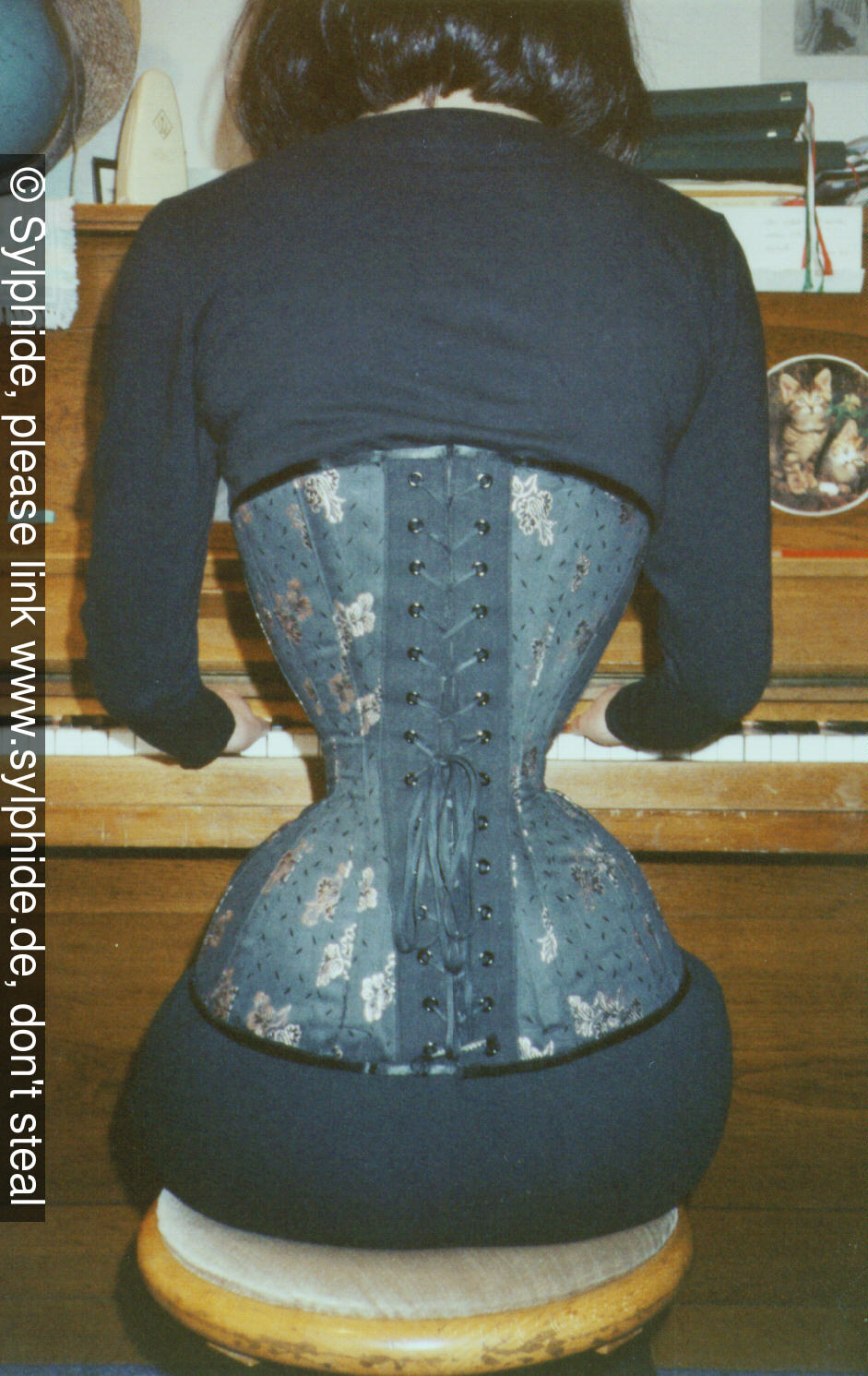 Brocade corset 18 inch tightlaced to wasp waist view sitting at the piano (back) Sylphide figure training tight lacing corset laced wasp waist tightlaced